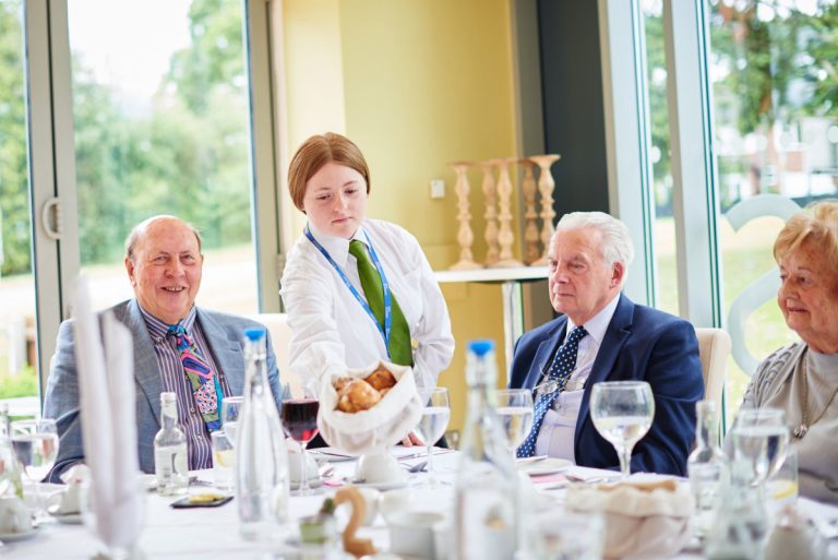 A hospitality student serves diners at Origins