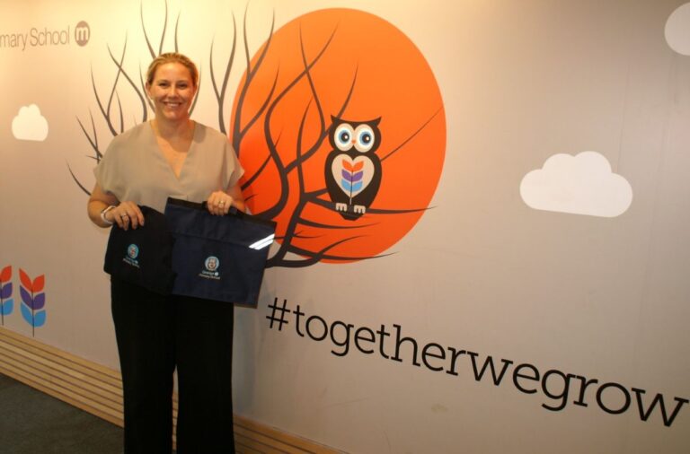 Head teacher Charlie Summers with school uniforms in front of the Grange Primary School’s logo